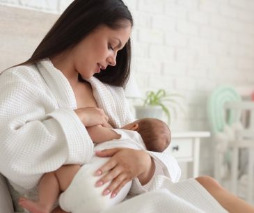 Mother in white robe breastfeeding her baby at home after breast surgery, illustrating post-operative nursing success