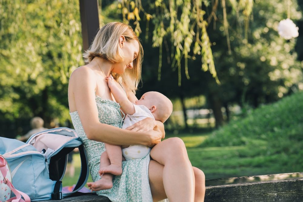 Mother breastfeeding her baby on a park bench, illustrating natural nipple changes after nursing