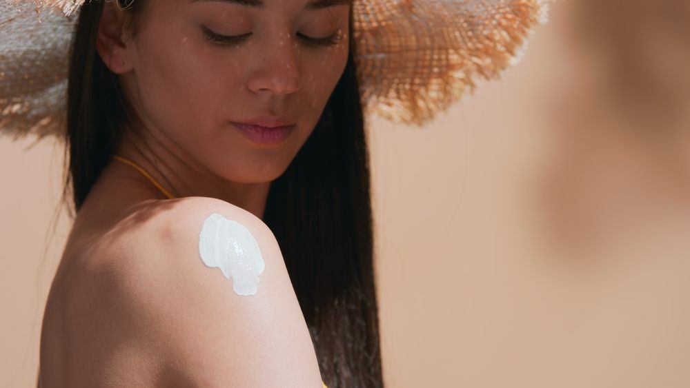 Woman applying sunscreen on shoulder to prevent summer sunburn and protect skin