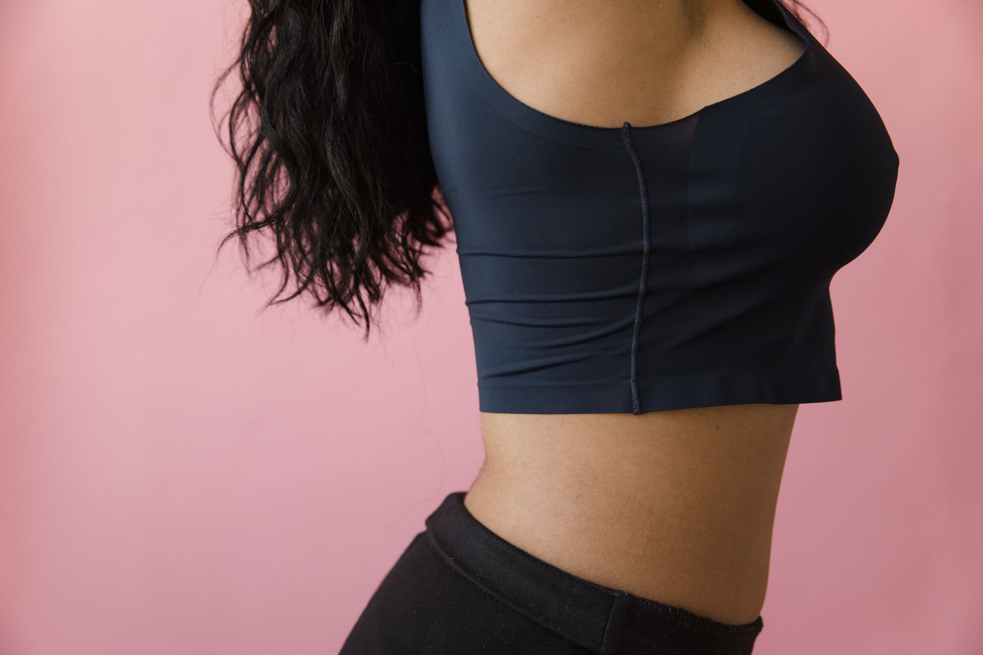 Side view of a woman in a blue crop top standing against a pink background.